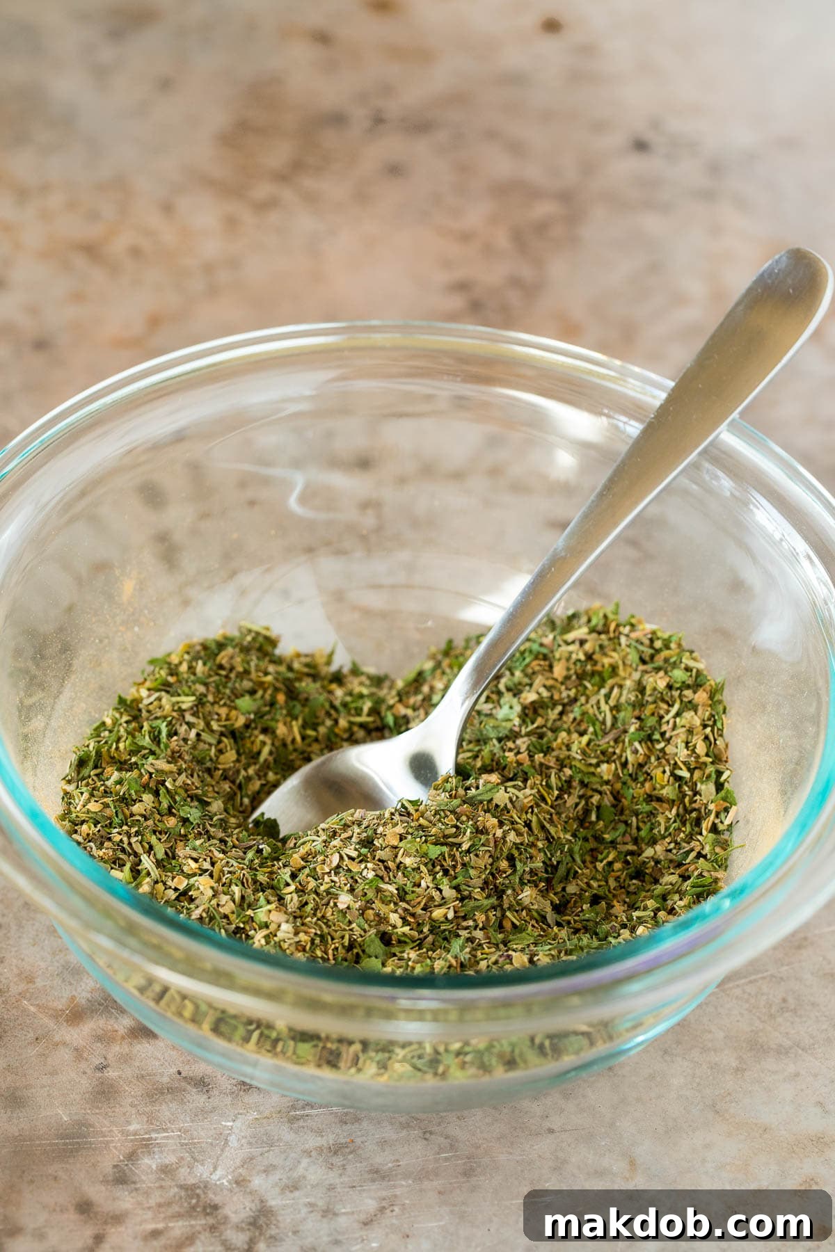 A bowl of Greek seasoning with a spoon in it, ready for use.