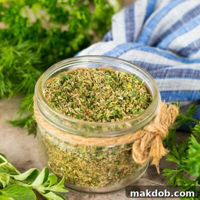 A jar of Greek seasoning surrounded by fresh herbs.