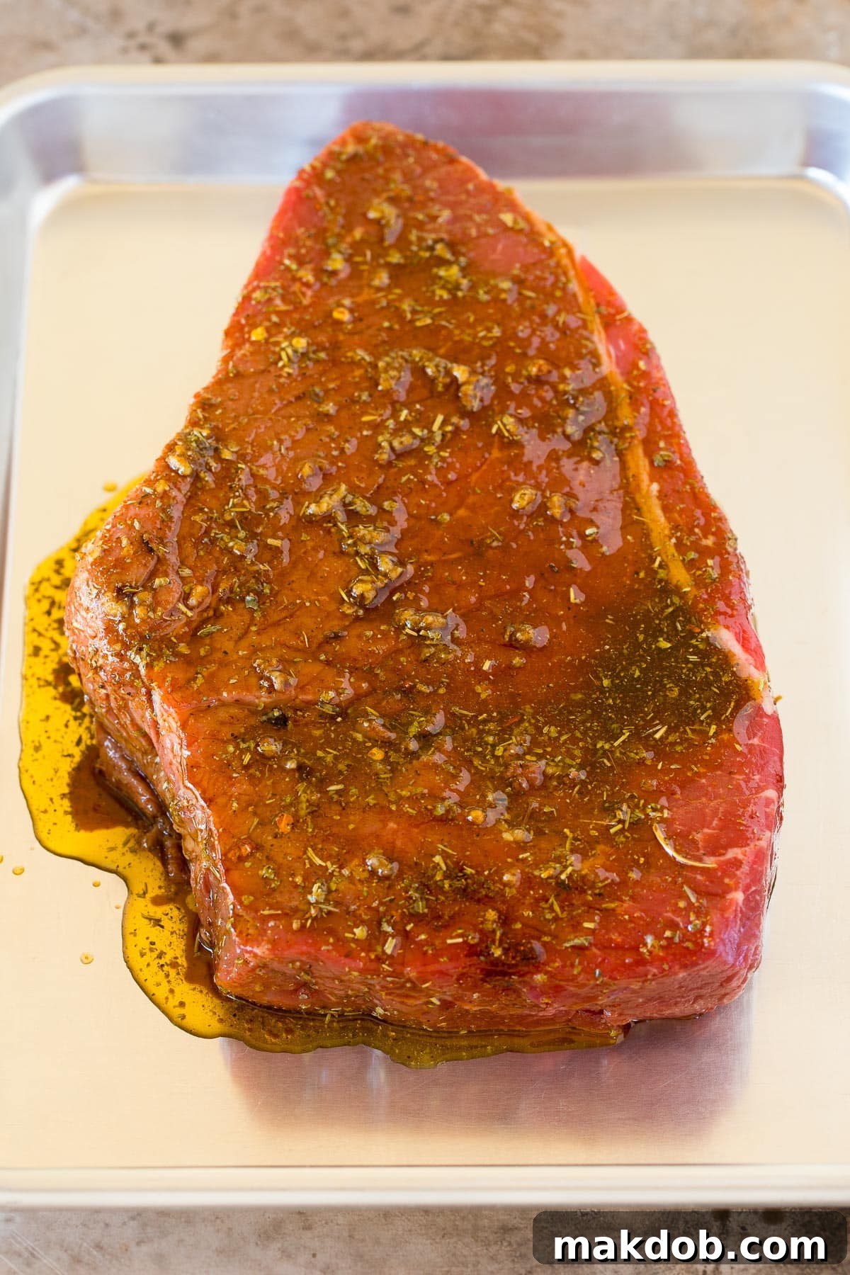 A large piece of marinated beef roast perfectly positioned on a sheet pan, ready for cooking.