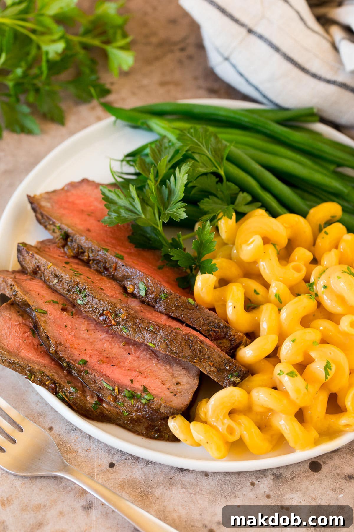 Perfectly sliced London broil served alongside creamy mac and cheese and vibrant green beans, creating a wholesome and appealing meal.