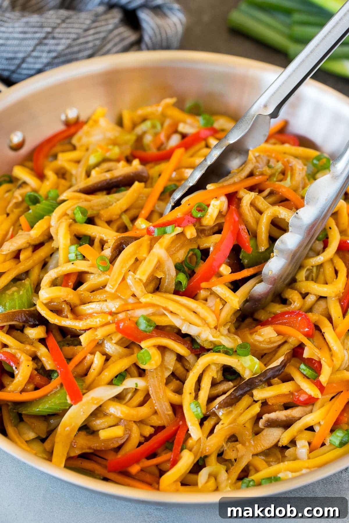 Vibrant Vegetable Lo Mein 6 Close-up of tongs lifting a generous portion of freshly made vegetable lo mein from a pan, highlighting the perfectly coated noodles and colorful vegetables.