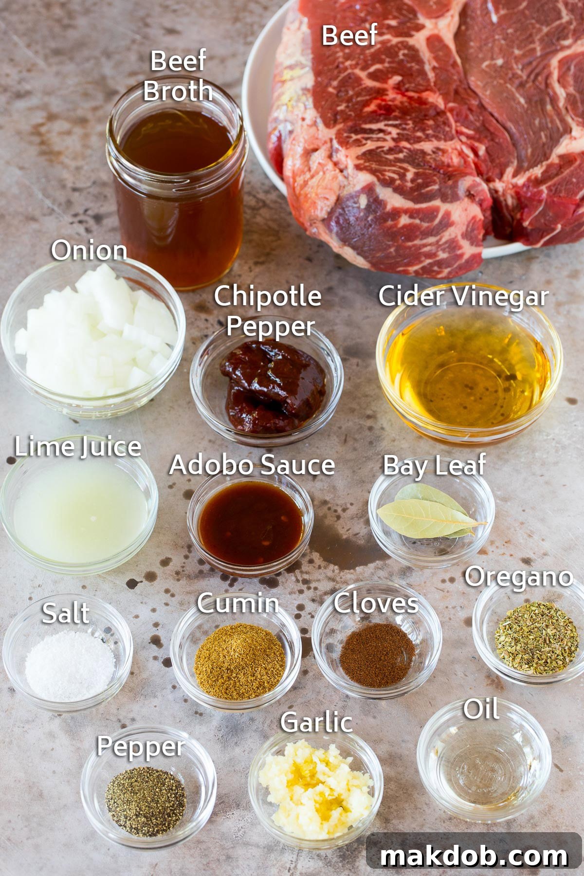 Bowls of different spices and seasonings including cumin, oregano, and cloves, next to a beef chuck roast.