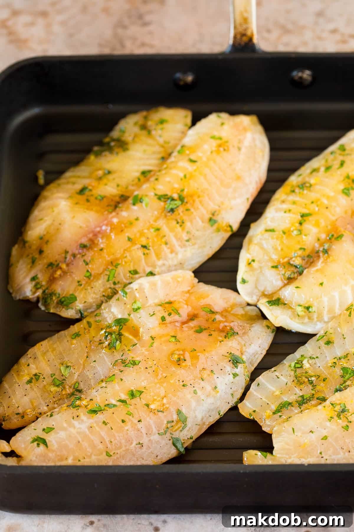 Marinated tilapia fillets sizzling on a hot grill pan, showcasing perfect sear marks.