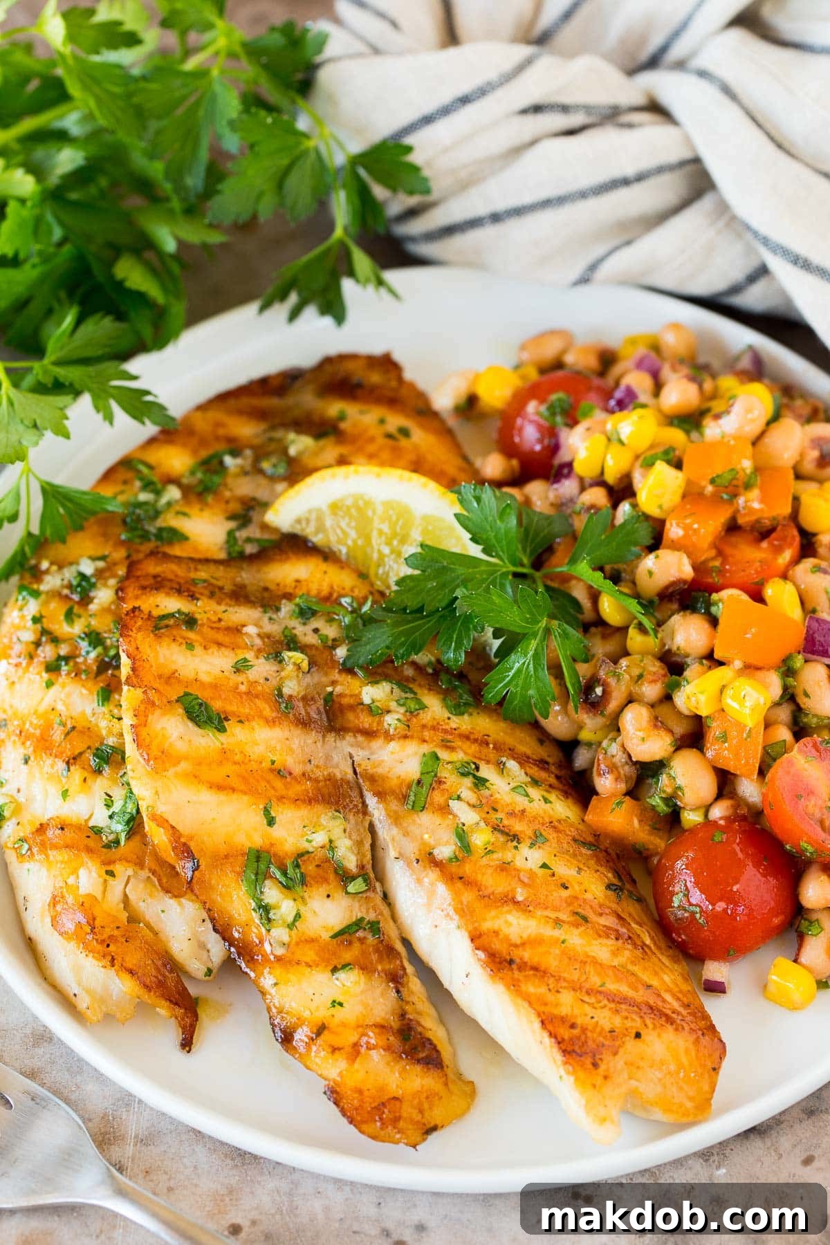 A perfectly grilled tilapia fillet served on a plate alongside a vibrant black-eyed pea salad, garnished with fresh herbs.