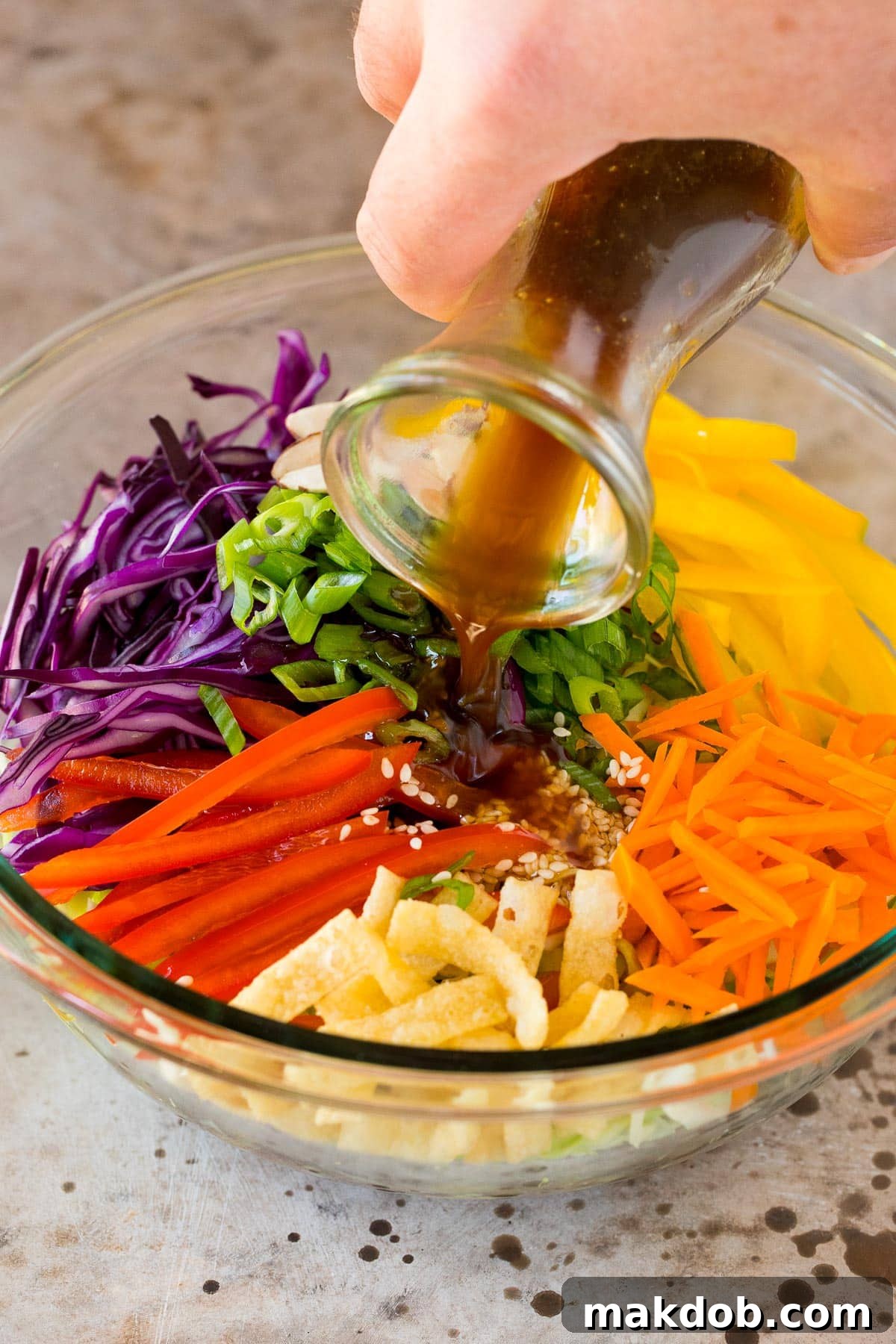 A vibrant, fresh salad with crisp greens and colorful vegetables being drizzled generously with homemade Asian salad dressing from a small pitcher.