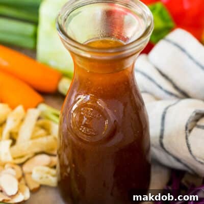 A jar of Asian salad dressing surrounded by vegetables.
