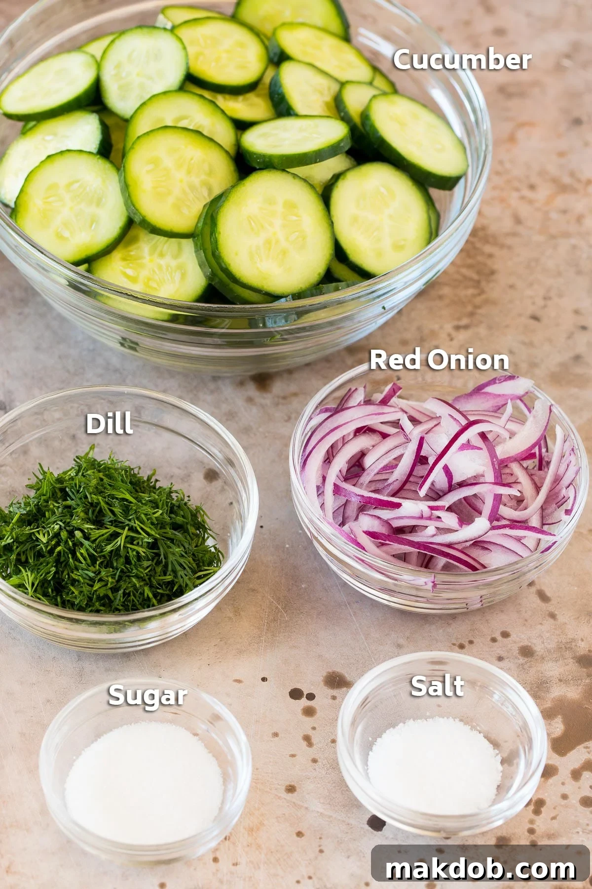 Bowls containing cucumbers, onion, dill, sugar and salt.