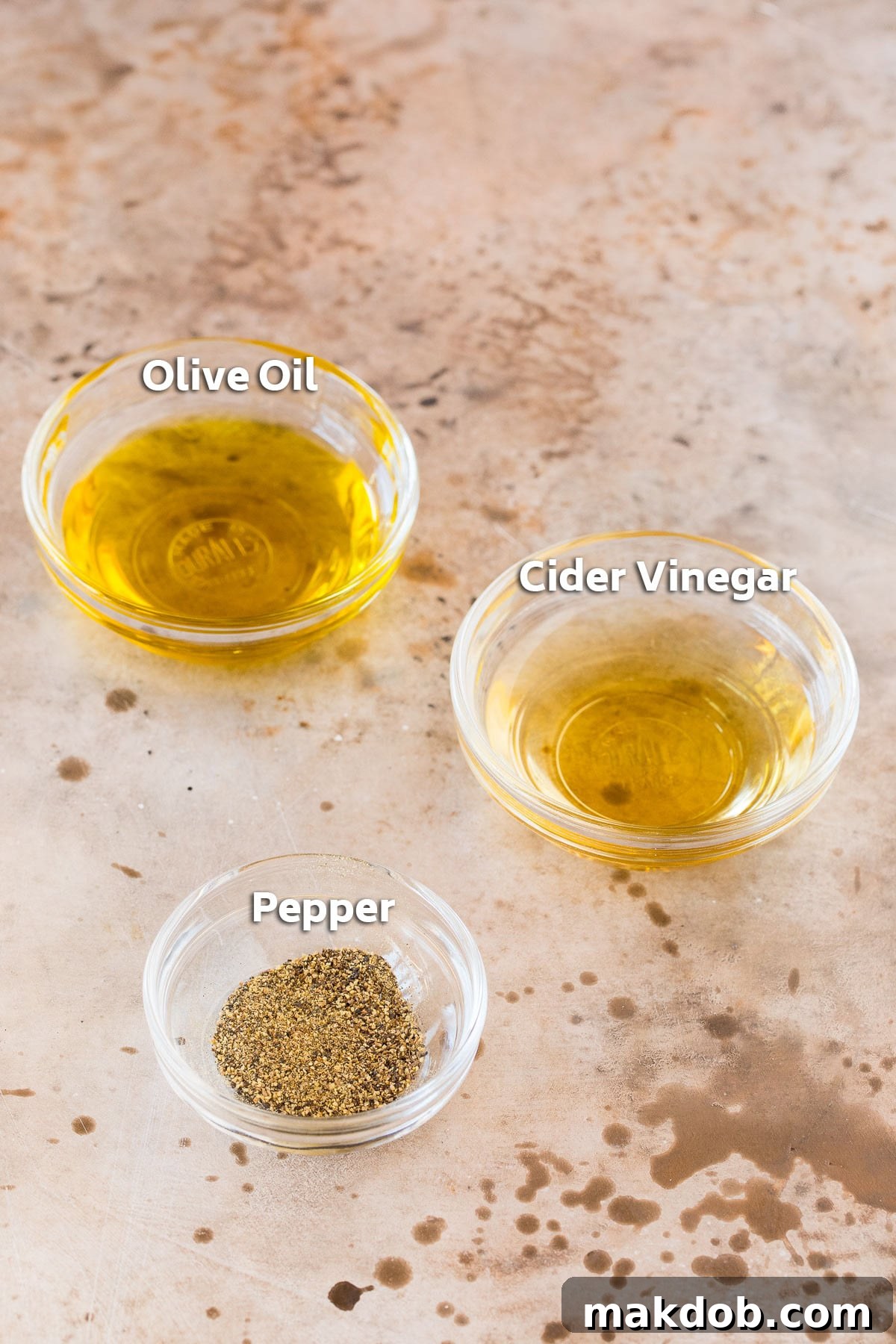 Small bowls containing the ingredients for the homemade salad dressing: apple cider vinegar, olive oil, and ground black pepper.