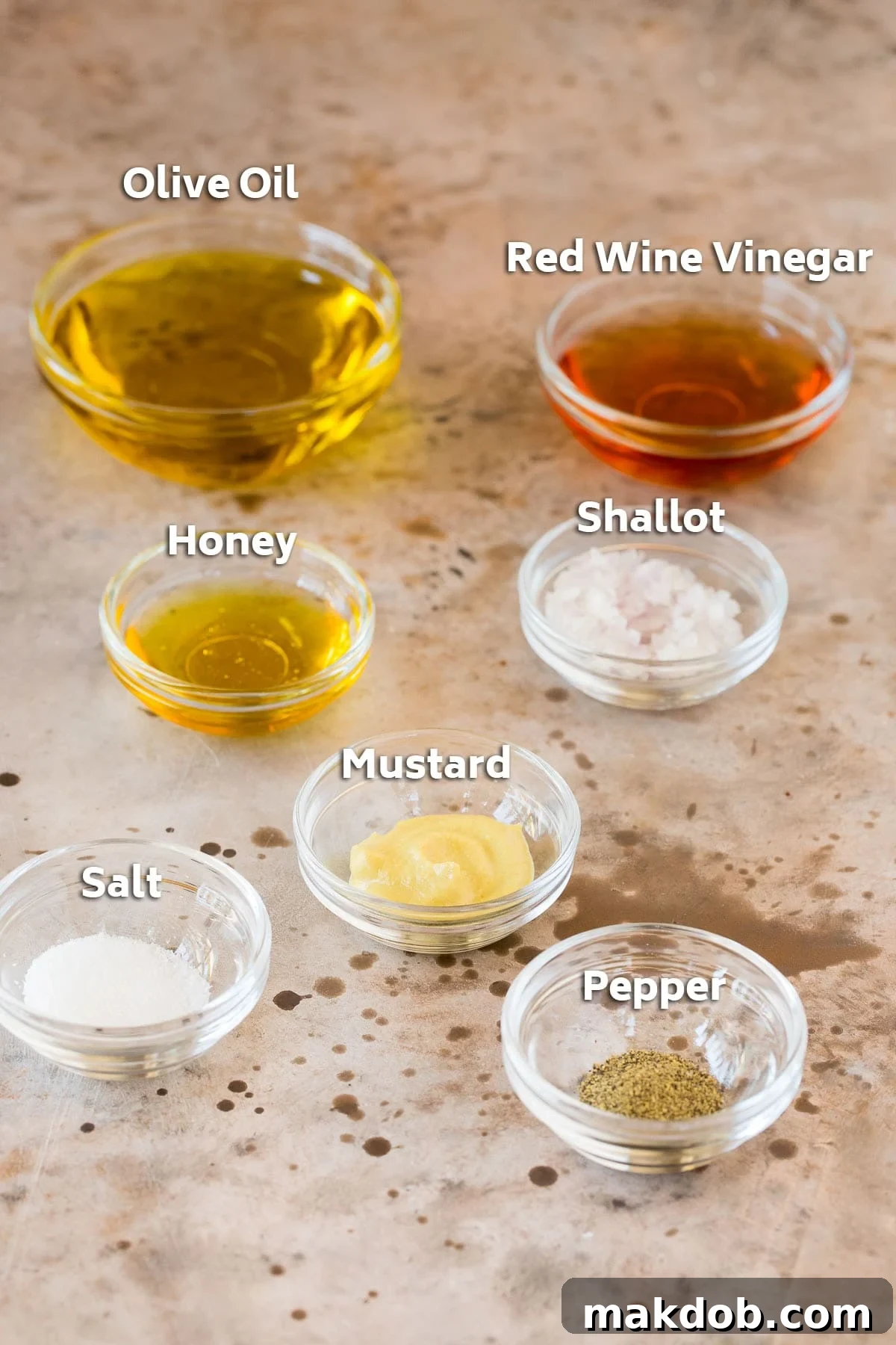 Small bowls containing the essential ingredients for a homemade salad dressing: glistening olive oil, red wine vinegar, minced shallots, honey, and Dijon mustard, ready to be whisked.