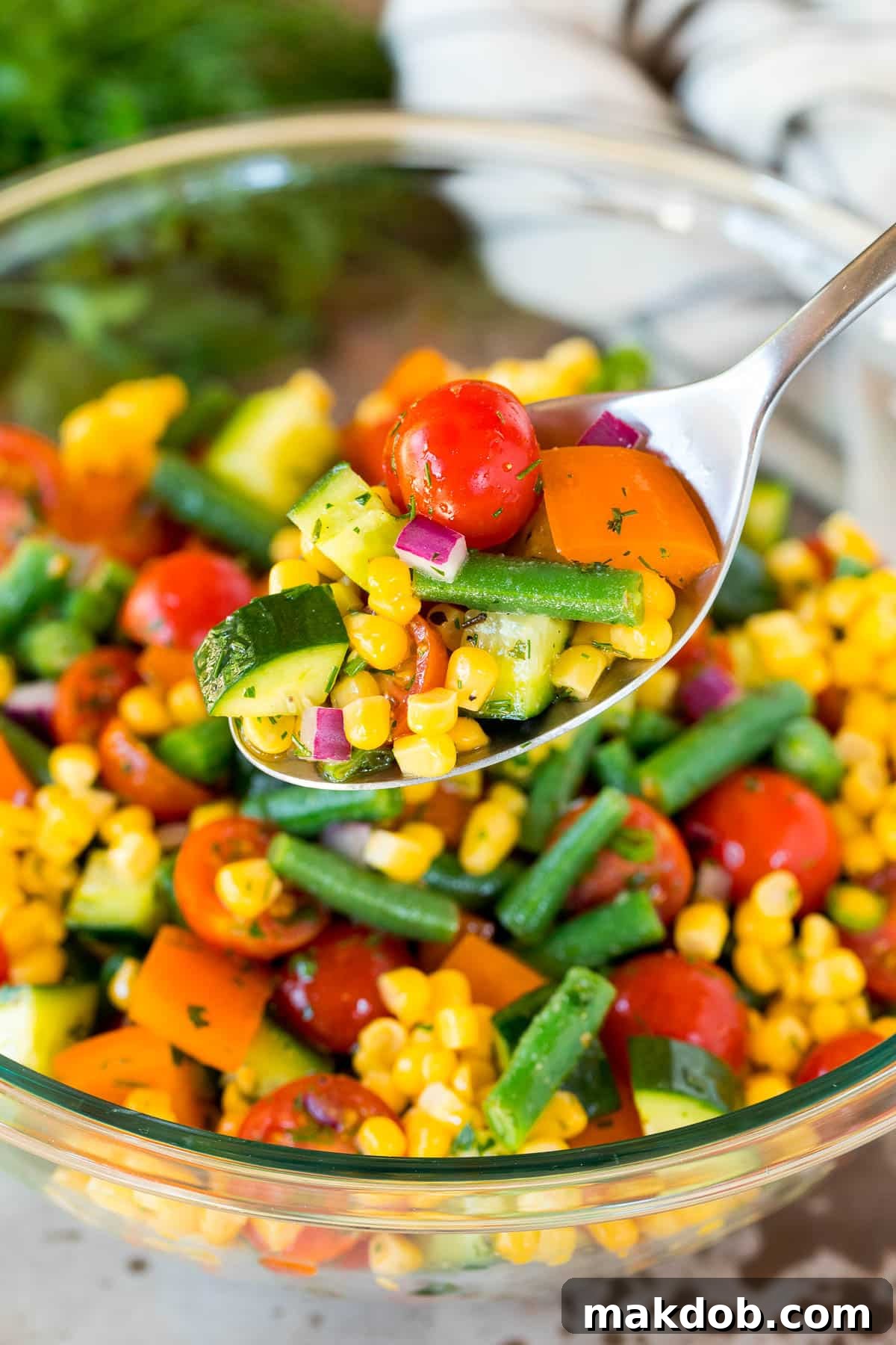 A serving spoon lifting a portion of colorful chopped vegetable salad from a large bowl, showcasing its fresh ingredients.