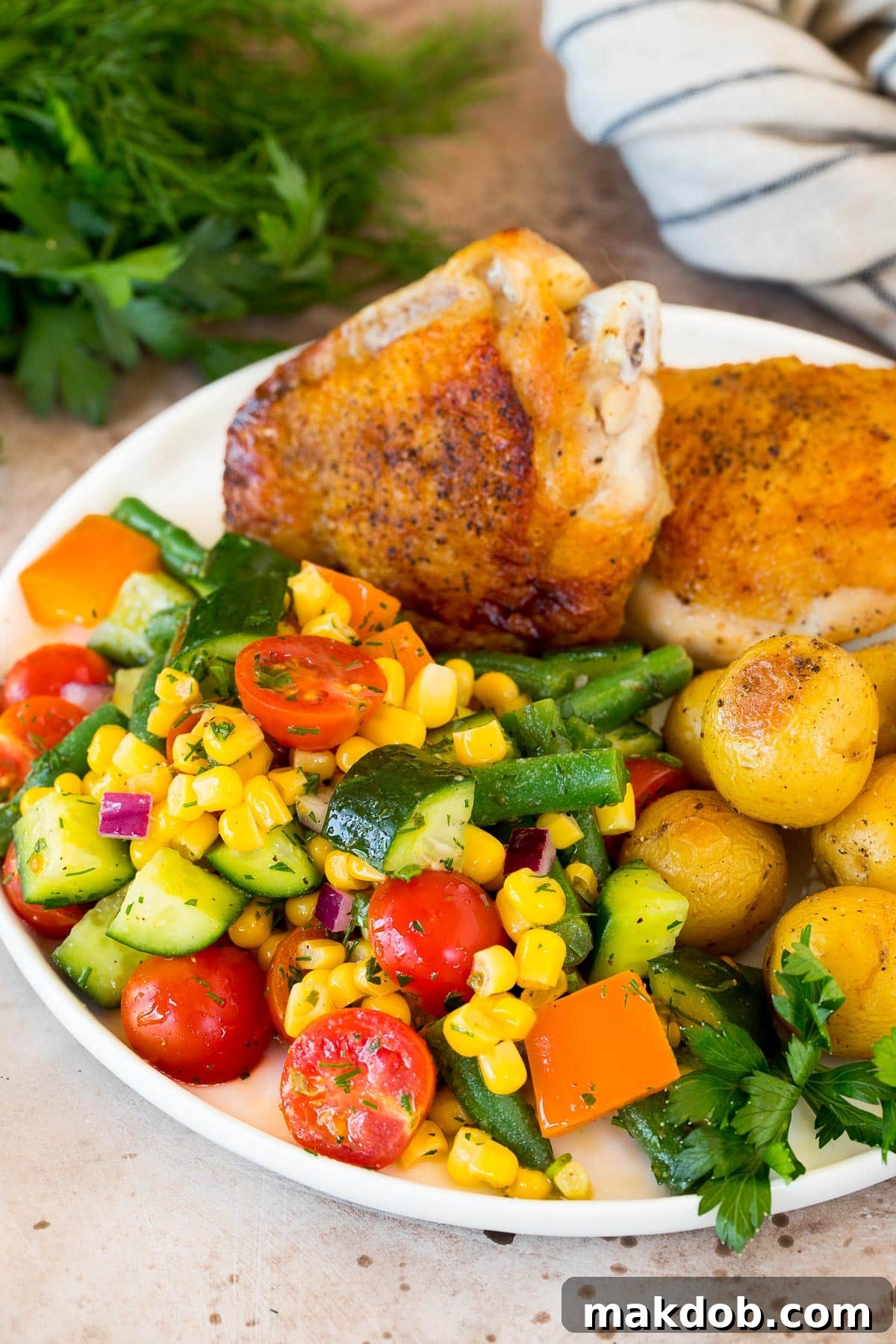 A full plate featuring a vibrant chopped vegetable salad served alongside grilled chicken and roasted potatoes, creating a complete and healthy meal.