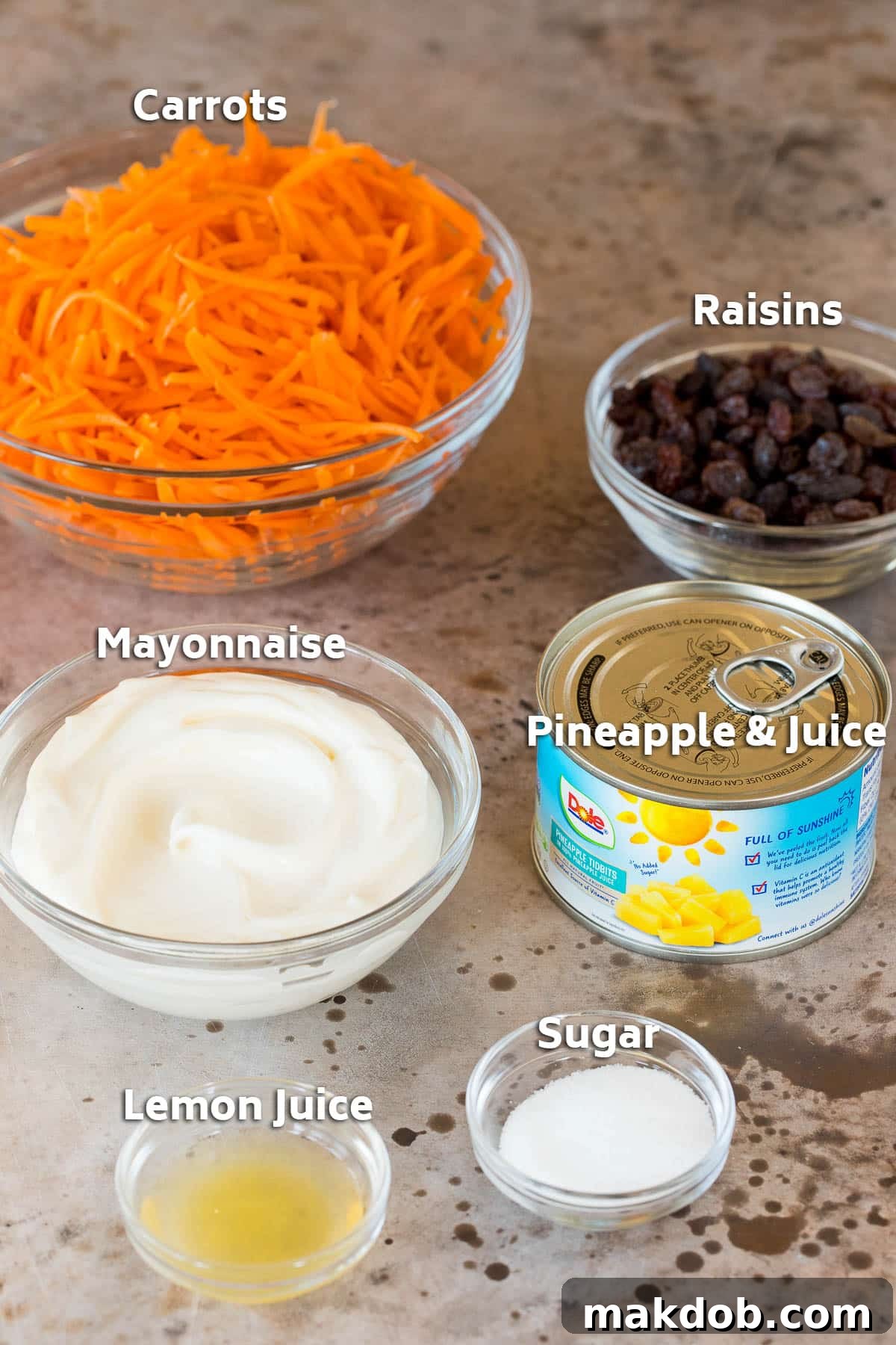 Individual bowls containing fresh shredded carrots, plump raisins, creamy mayonnaise, and zesty seasonings, ready for assembly.