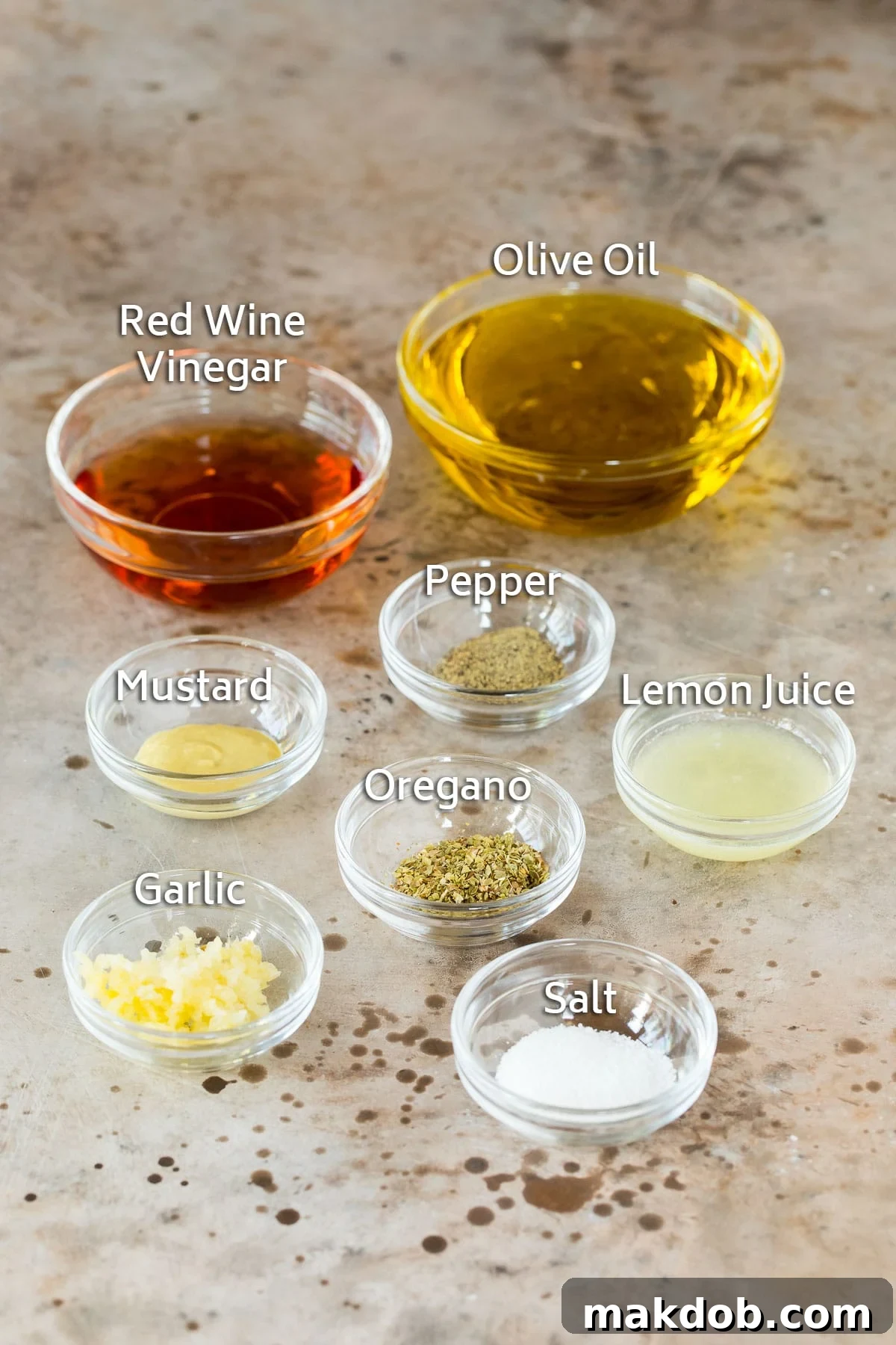 Small bowls containing the essential ingredients for Greek salad dressing: golden olive oil, deep red wine vinegar, bright lemon juice, and various herbs and spices.
