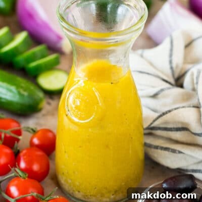 A bottle of Greek salad dressing surrounded by fresh vegetables.