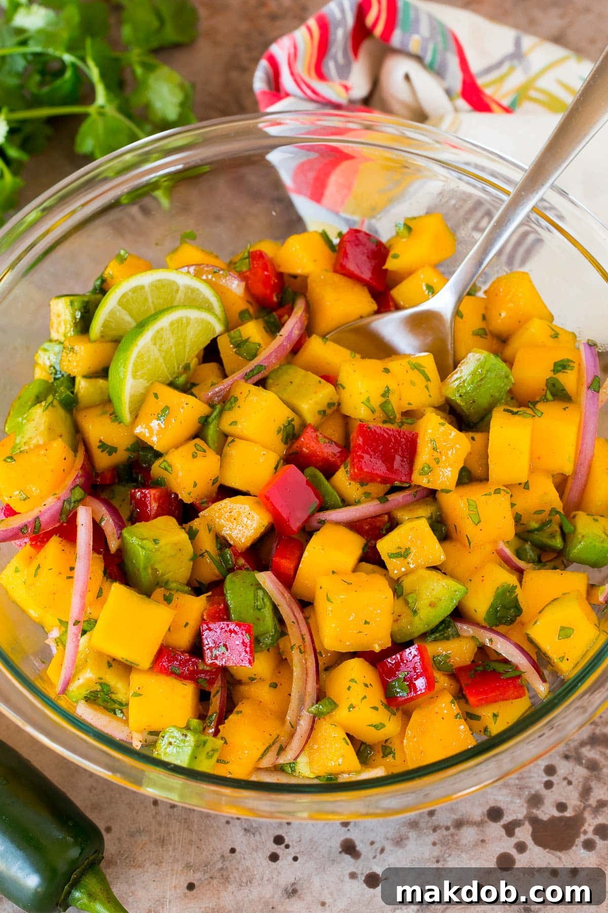 A bowl of vibrant mango salad with a serving spoon, showcasing diced fresh mango, avocado, red onion, and bell pepper.