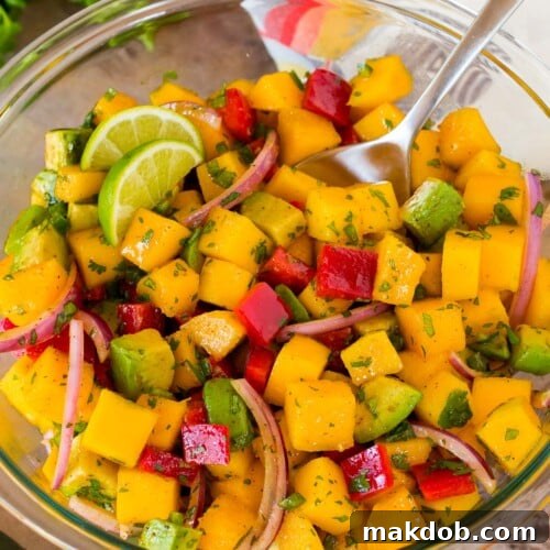 A bowl of mango salad with a serving spoon in it.