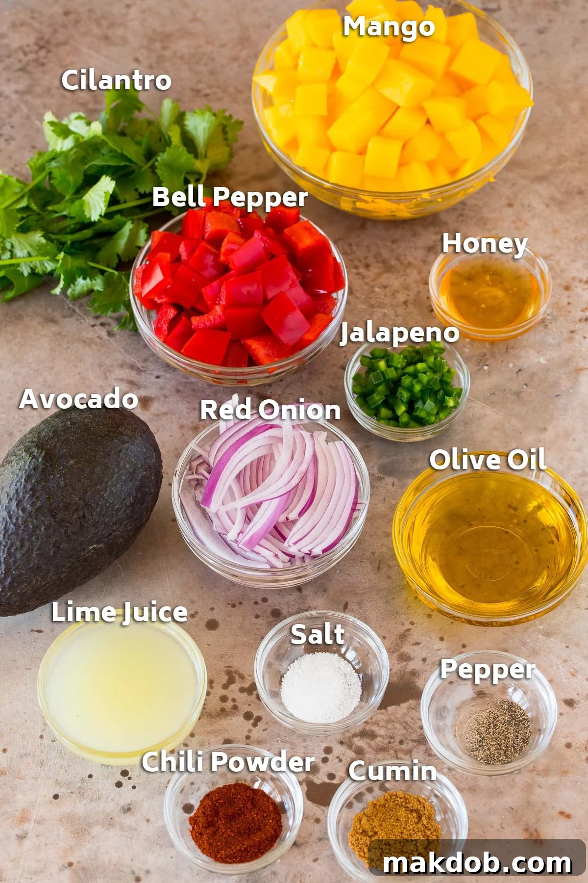 Bowls of fresh ingredients for mango salad, including diced mango, avocado, red onion, bell pepper, cilantro, lime juice, olive oil, honey, chili powder, cumin, salt, and pepper.