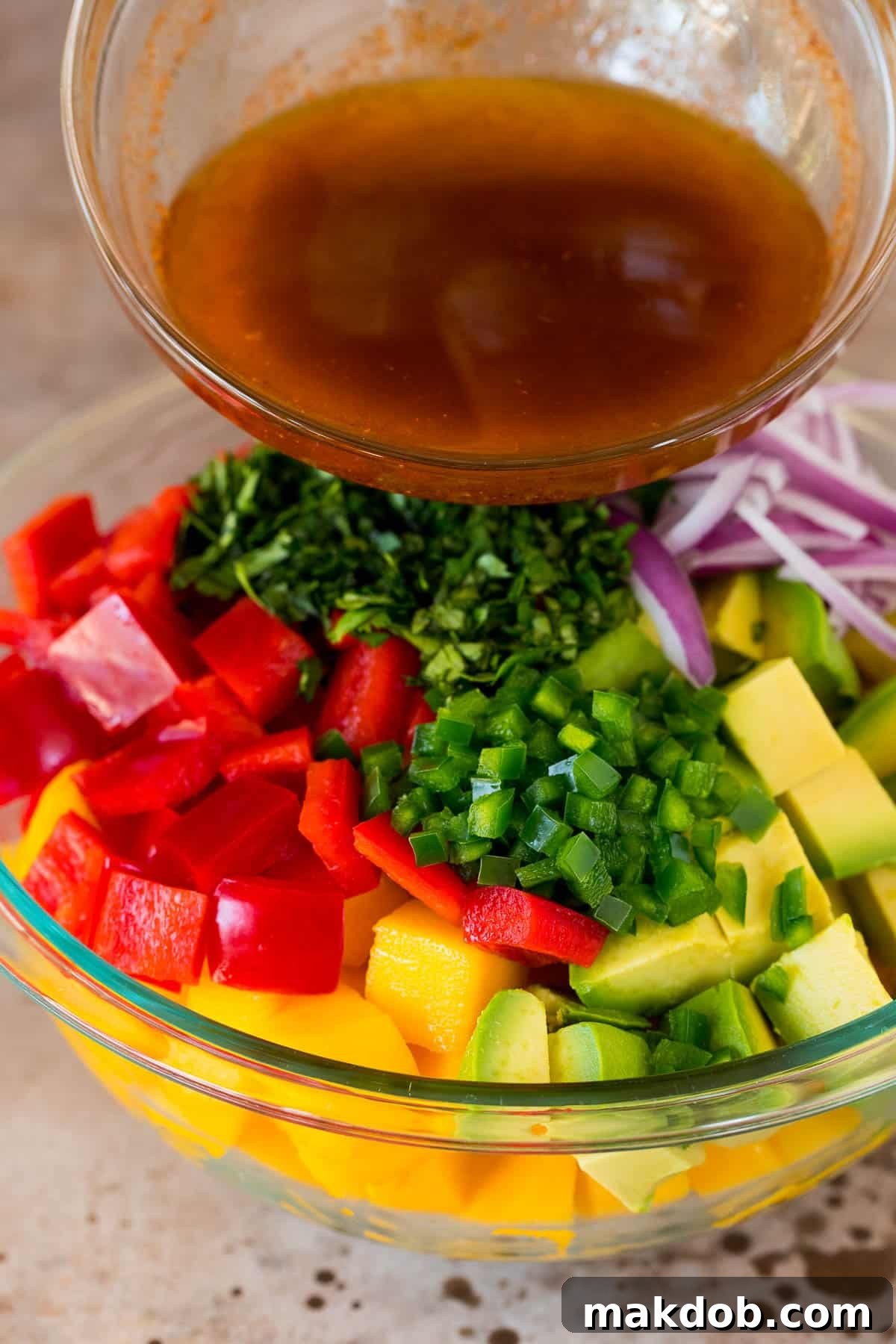 Pouring zesty homemade dressing over a bowl of fresh diced mango and vegetables for a vibrant salad.