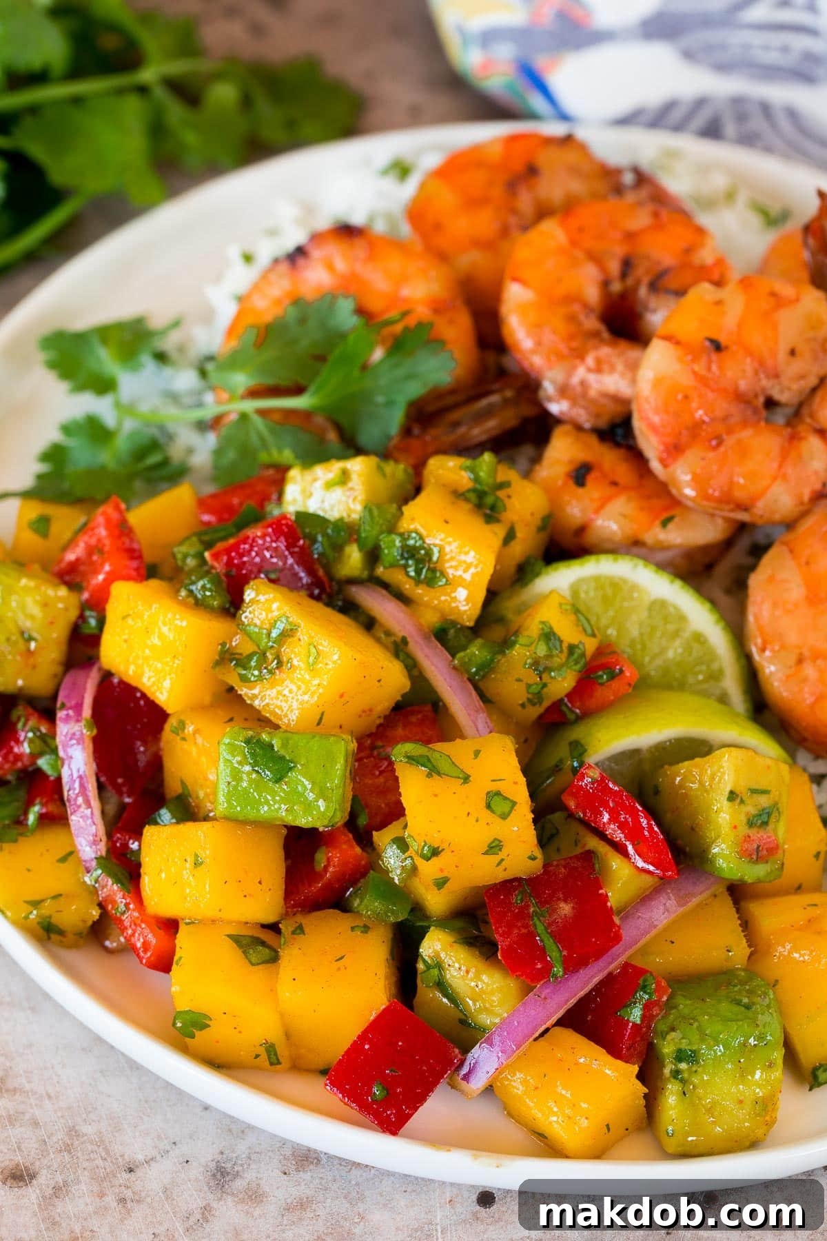 A serving of mango salad on a plate, beautifully garnished, next to grilled shrimp and a portion of fluffy rice.