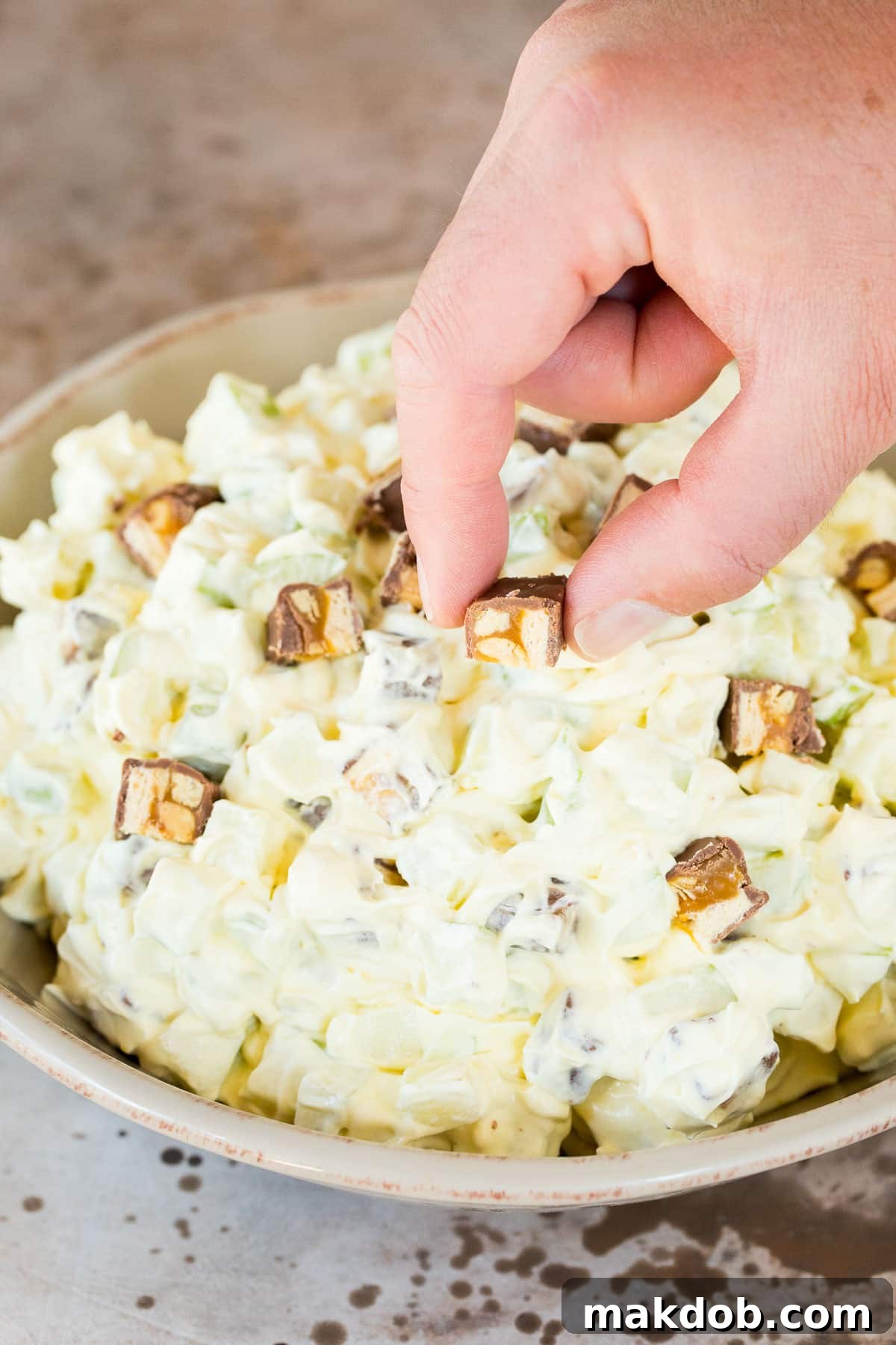 Snickers Apple Delight 5 A hand placing chopped candy bars on apple salad.