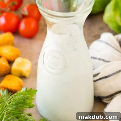 A glass container of homemade ranch dressing surrounded by salad ingredients.