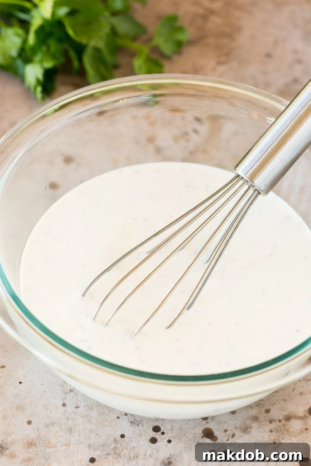 A bowl of creamy herb dressing with a whisk resting in it, showcasing its perfect texture.