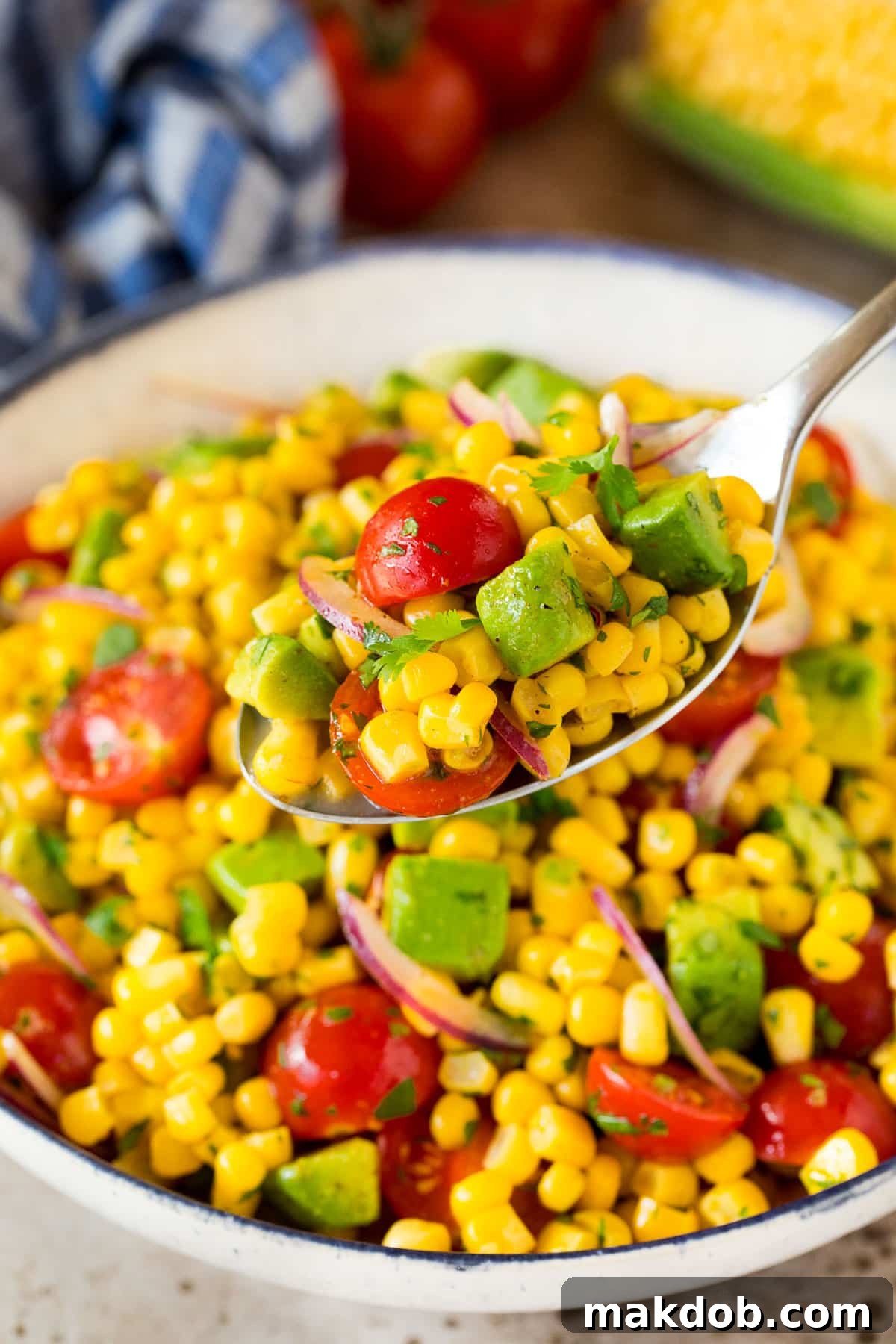 A spoon serving up a portion of salad made with avocado and corn.