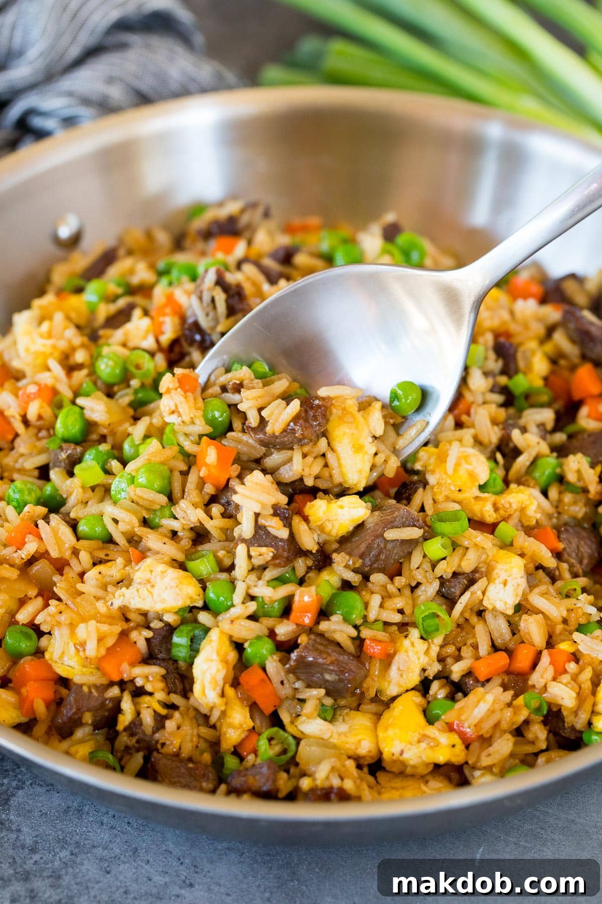 A large pan filled with freshly cooked beef fried rice, a serving spoon resting within the flavorful mixture.