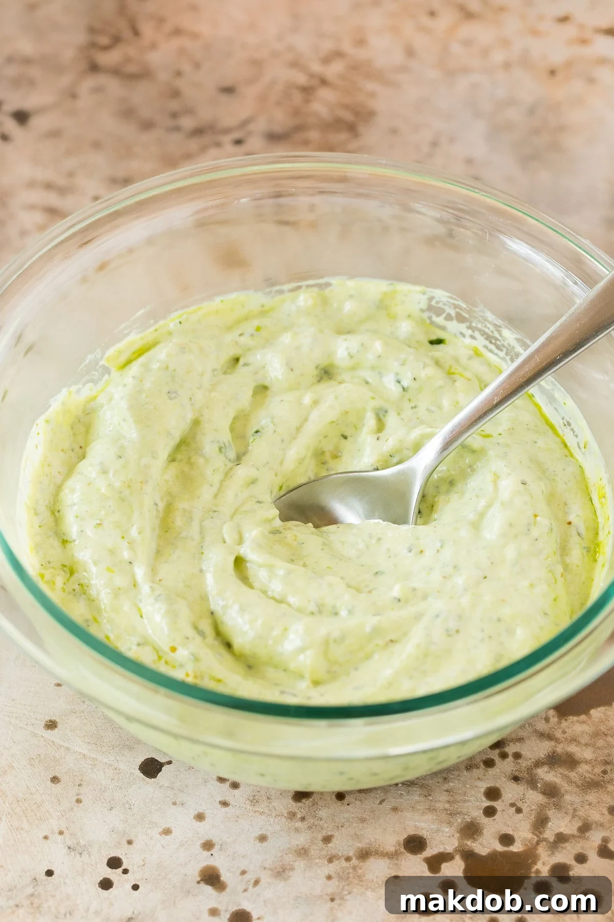 A close-up view of the perfectly blended creamy pesto dip in a white bowl, showcasing its smooth texture and rich green color, highlighting the harmonious combination of pesto, mayonnaise, and sour cream.