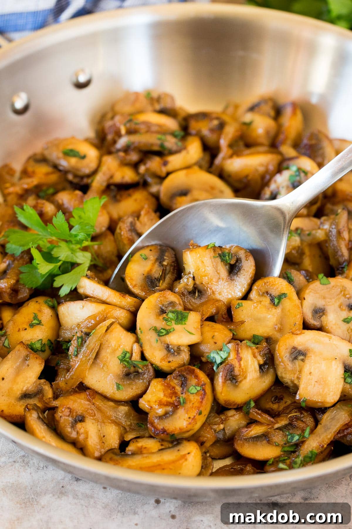 Golden Sauteed Mushrooms and Onions 2 A serving spoon lifting a portion of glistening, golden-brown sautéed mushrooms and onions from a pan.