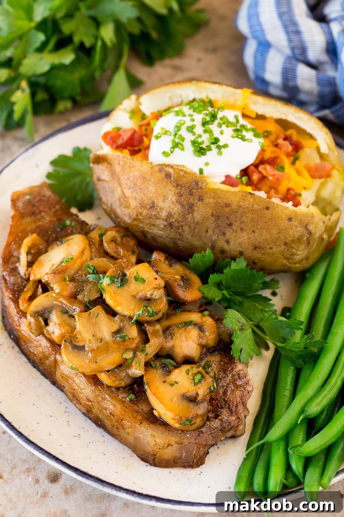 Golden Sauteed Mushrooms and Onions 6 A generous serving of sautéed mushrooms and onions elegantly placed atop a juicy steak, with a baked potato and green garnish completing the plate.