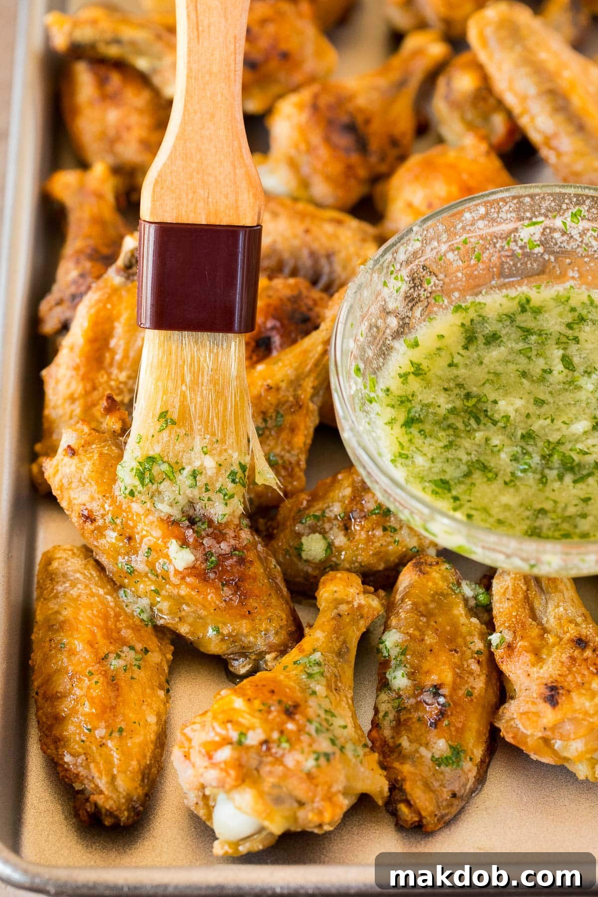 A kitchen brush coating crispy chicken wings with garlic butter sauce, showing the glistening, flavorful coating.