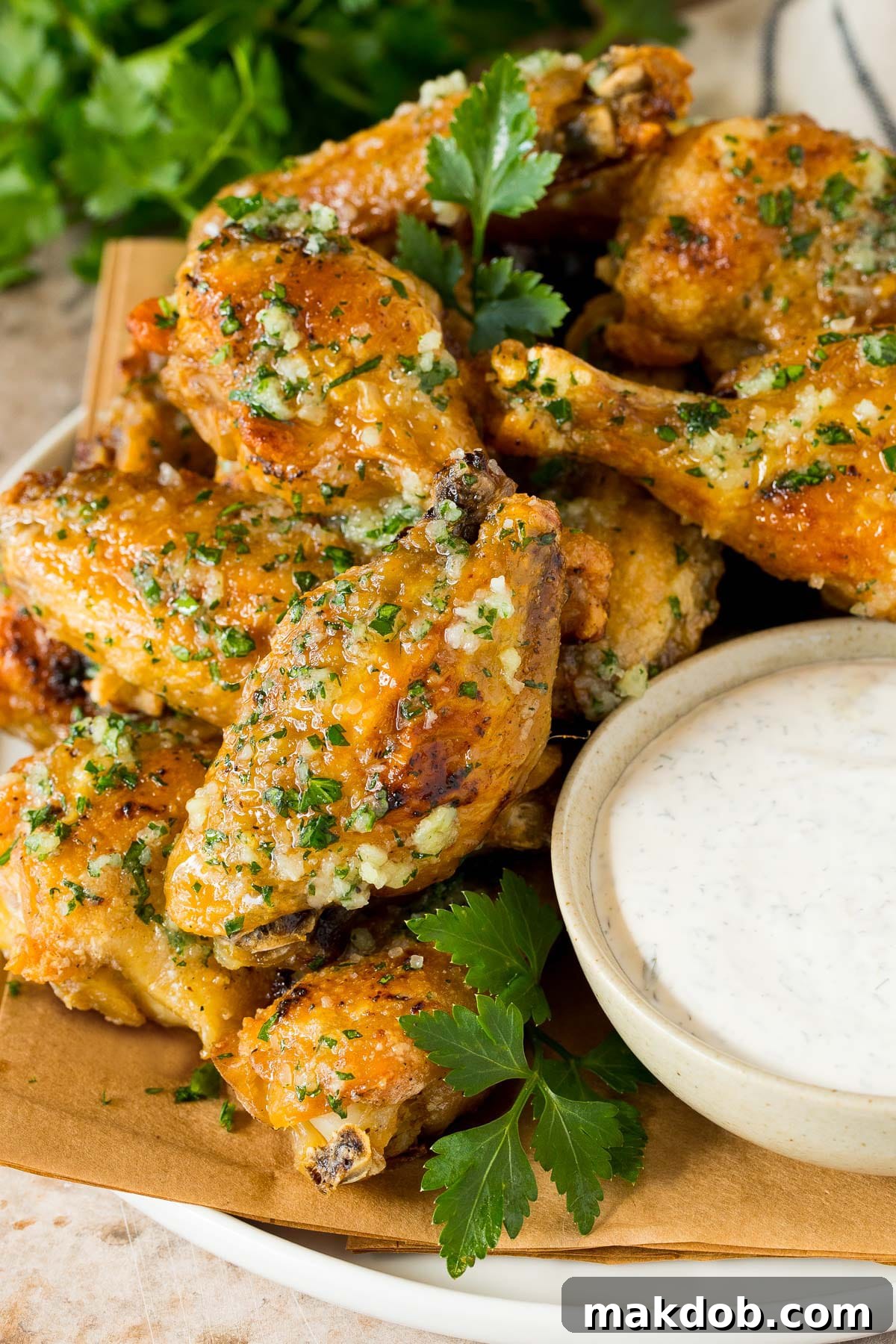 A plate of garlic parmesan wings served with a side of creamy ranch dressing and fresh parsley garnish.