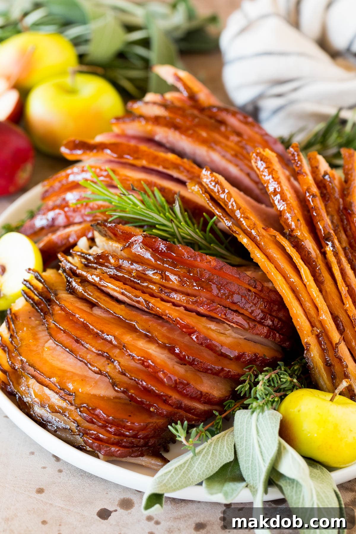 Sweet Glazed Easter Ham 6 Perfectly sliced Easter ham on a plate, beautifully garnished with fresh herbs and apple slices.