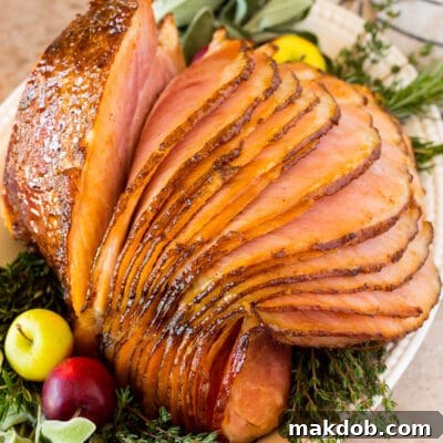 A glazed Easter ham on a platter garnished with herbs and apples.
