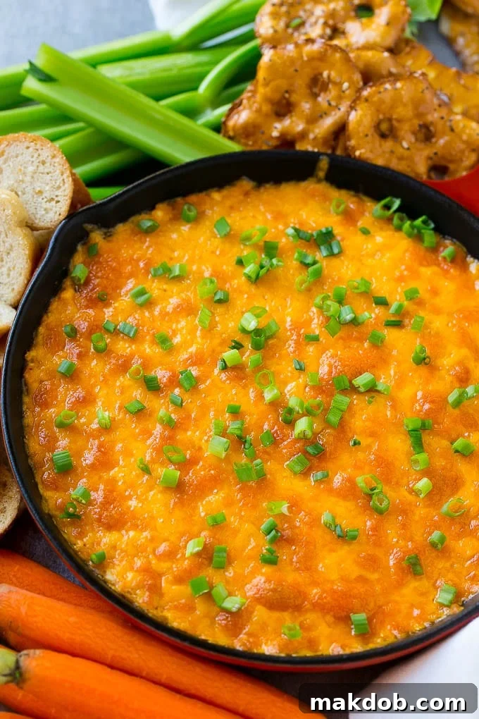 Buffalo Ranch Chicken Dip | Buffalo Chicken Dip | Baked Buffalo Dip | Cheesy Buffalo Dip #buffalowings #buffalochicken #dip #lowcarb #appetizer #dinneratthezoo Buffalo ranch chicken dip topped with melted cheese and green onions, surrounded by vegetables, pretzels and baguette slices.
