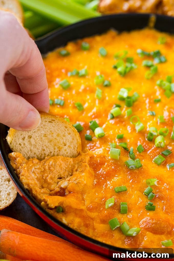 Buffalo Ranch Chicken Dip | Buffalo Chicken Dip | Baked Buffalo Dip | Cheesy Buffalo Dip #buffalowings #buffalochicken #dip #lowcarb #appetizer #dinneratthezoo Baked buffalo chicken dip with a baguette slice scooping some out.