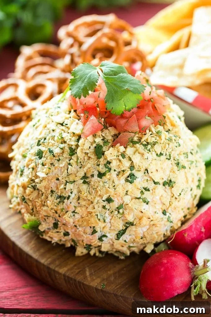A jalapeno cheese ball coated in tortilla chips and topped with diced tomatoes, ready to be served.