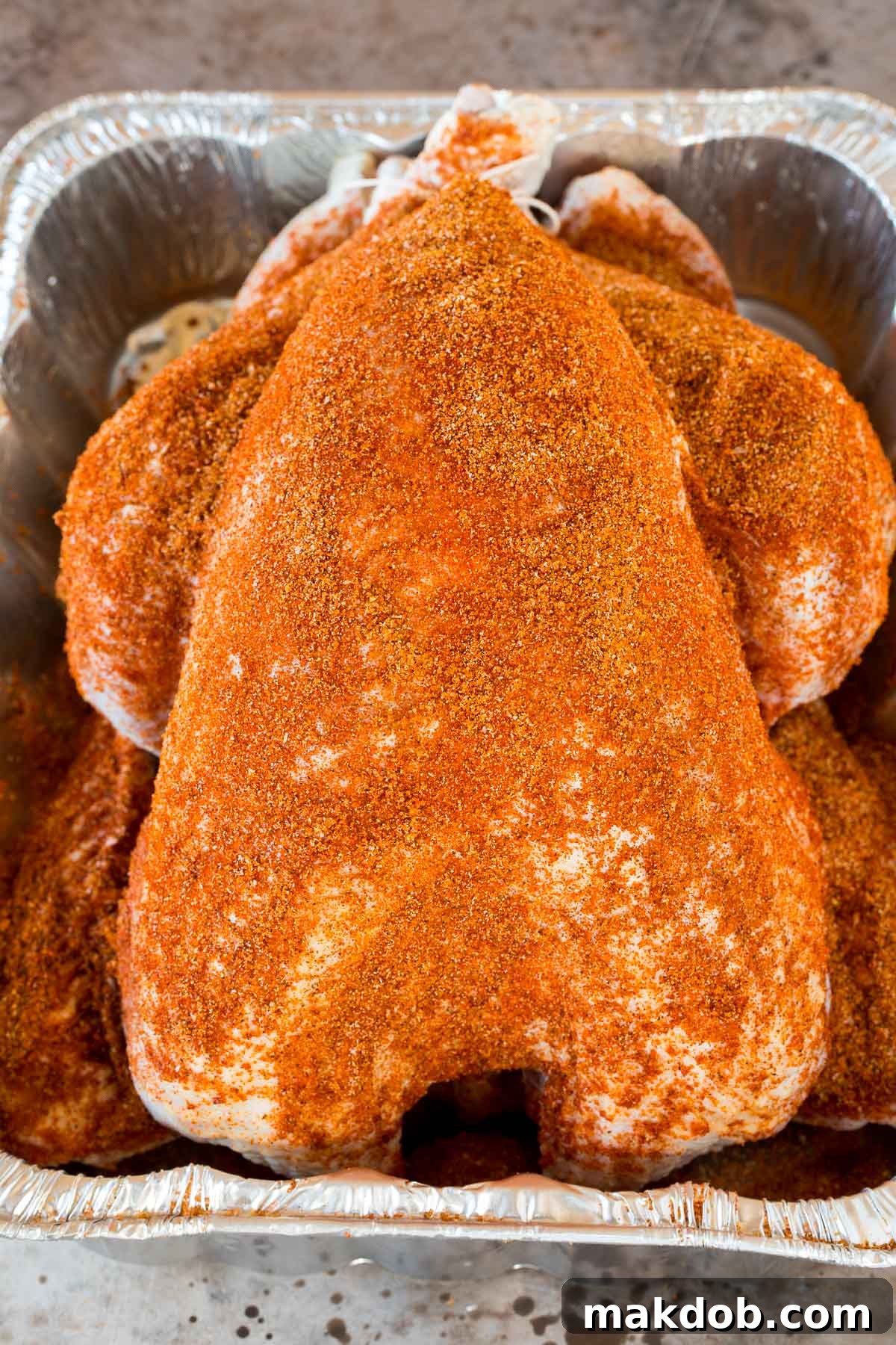 A raw whole turkey, generously coated with the homemade smoked turkey rub, resting in a roasting pan, ready for the smoker.