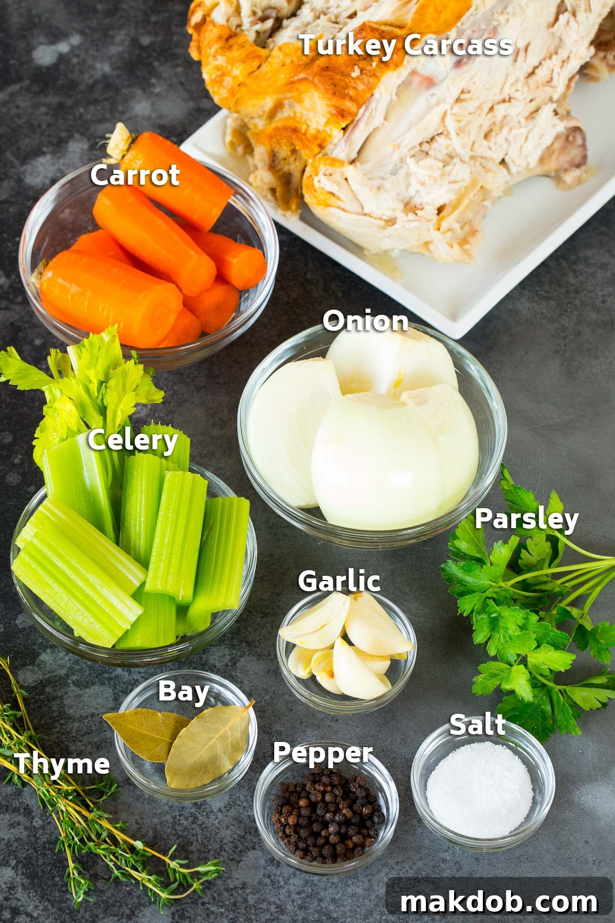 Assorted ingredients neatly arranged, ready to be used for making a pot of homemade turkey broth, including a turkey carcass, vegetables like onion, carrots, and celery, and fresh herbs.