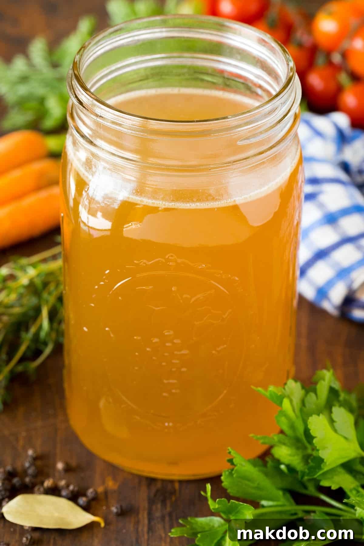 Homemade Turkey Broth A jar of homemade turkey broth surrounded by herbs and vegetables.