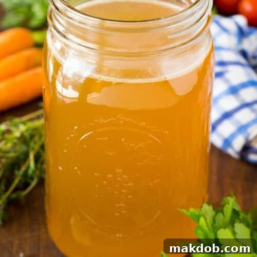 A jar of homemade turkey broth surrounded by herbs and vegetables.