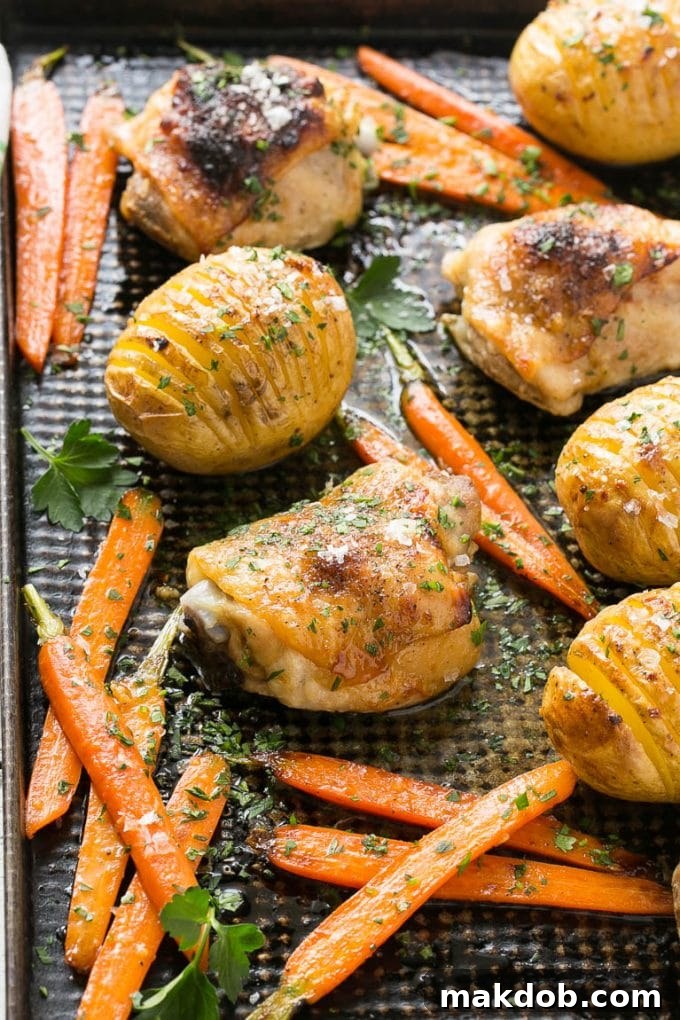 A sheet pan with perfectly roasted maple dijon chicken, golden hasselback potatoes, and caramelized carrots.