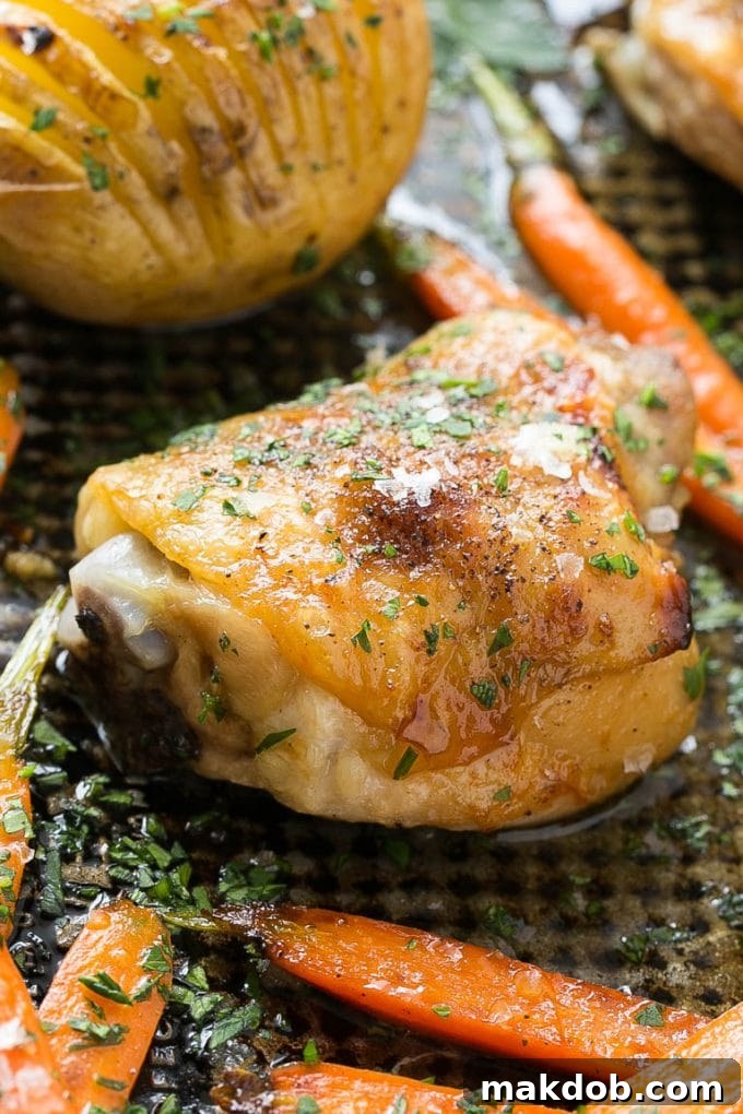 A roasted chicken thigh served with hasselback potatoes and roasted carrots, glistening with maple dijon glaze.