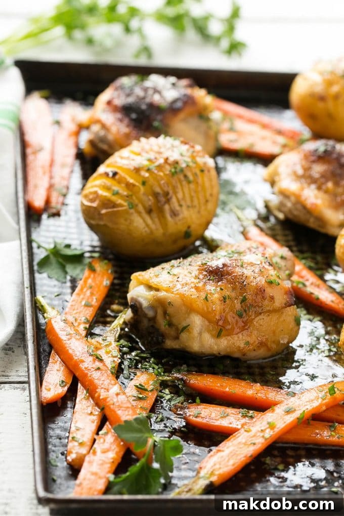 A close-up of a pan filled with golden-brown maple dijon chicken, fanned hasselback potatoes, and roasted carrots.