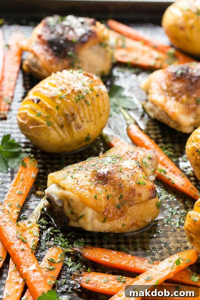 Close-up of perfectly roasted hasselback potatoes with maple dijon chicken on a sheet pan.