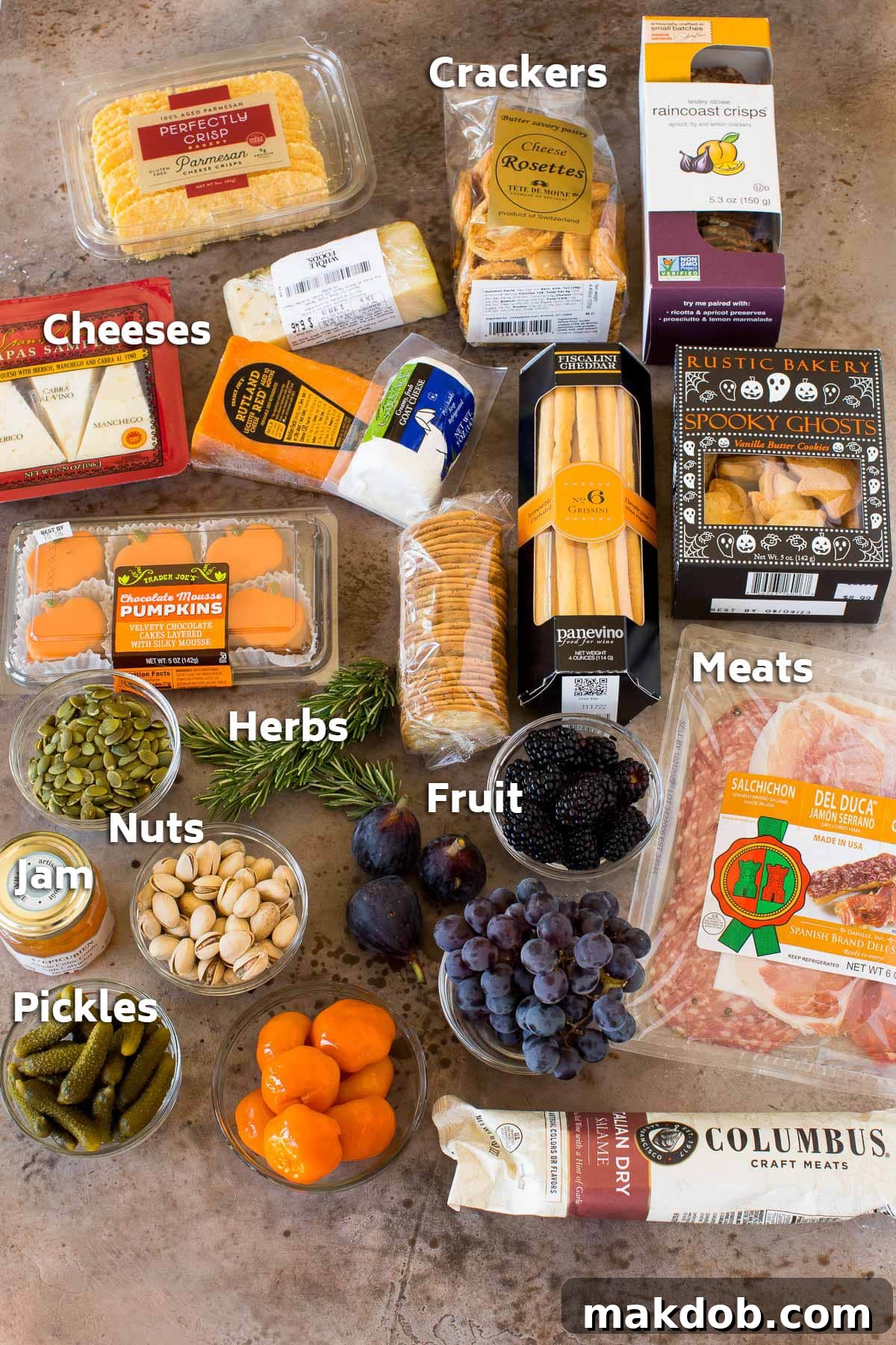 Ingredients for a Halloween charcuterie board, including various packages of crackers, cured meats, and blocks of cheese.