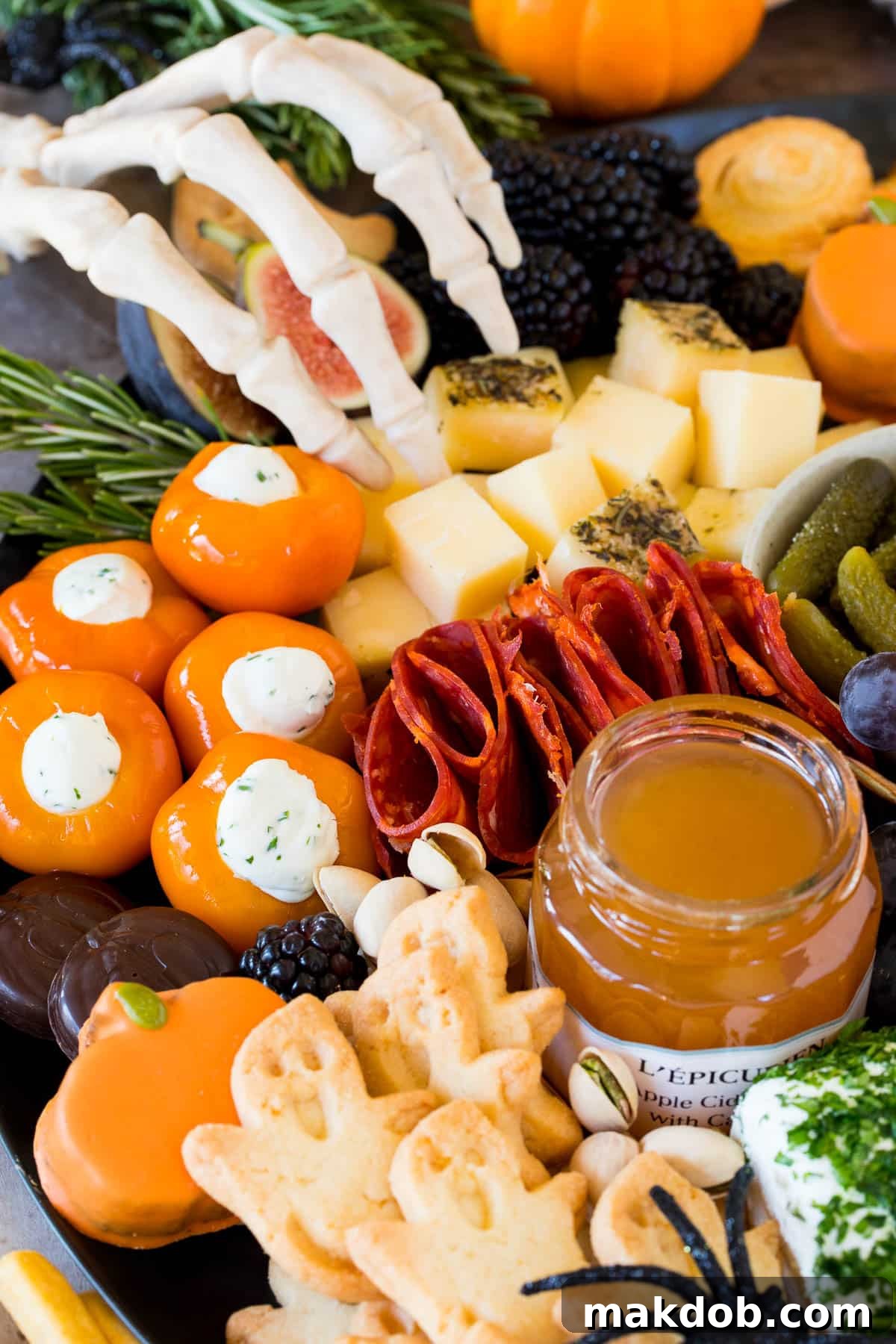 A close up shot of a Halloween charcuterie board with ghost cookies, various meats, and a pot of jam.