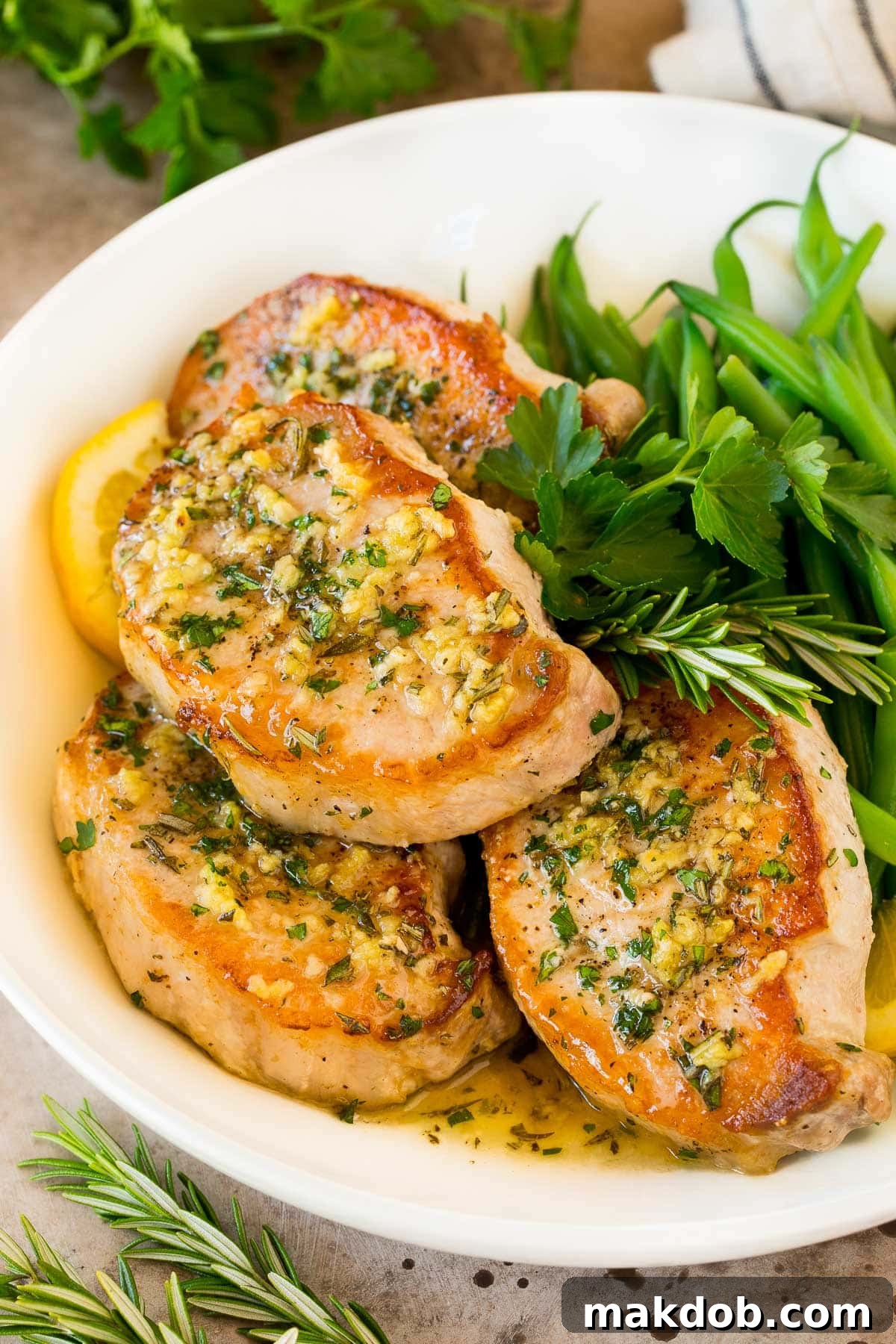 Beautifully baked boneless pork chops arranged on a serving platter, garnished with fresh herbs and accompanied by vibrant green beans.