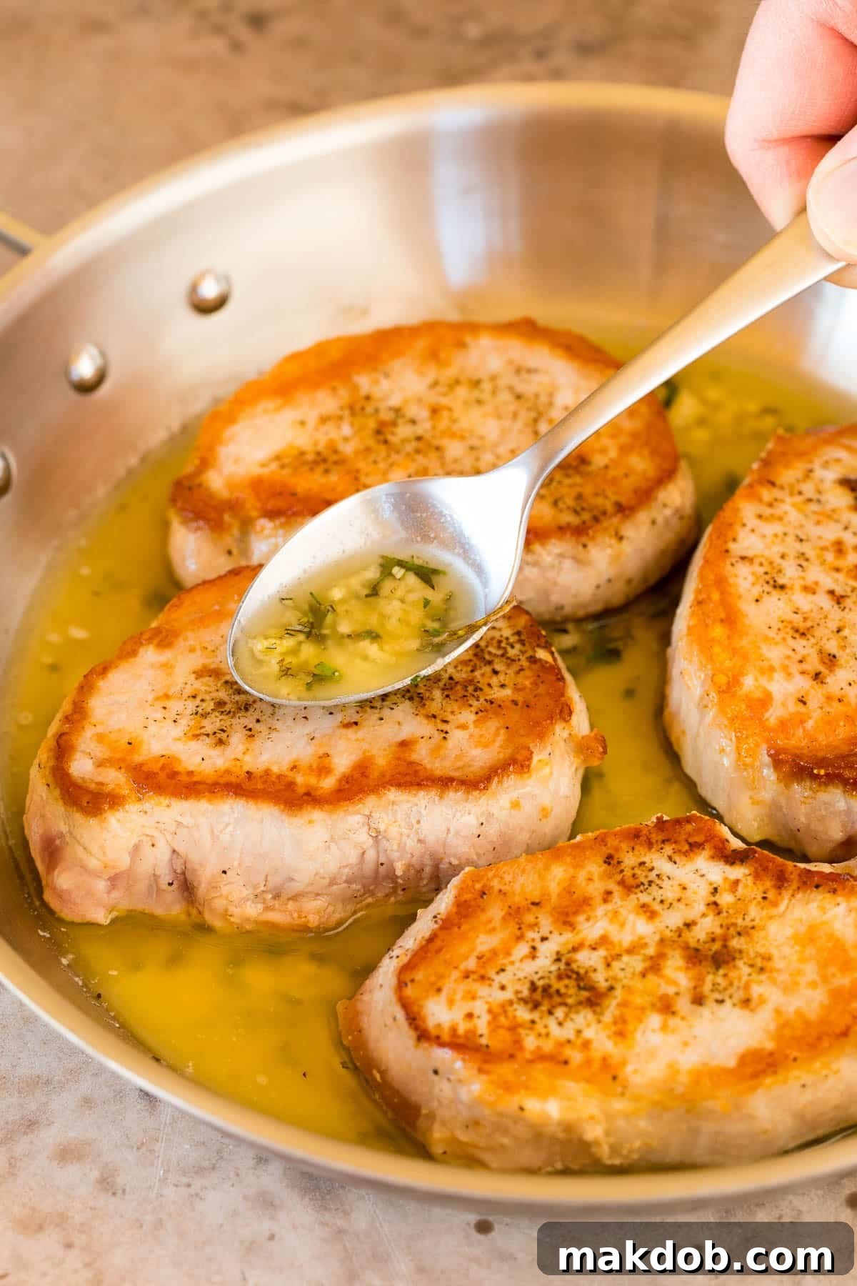 A close-up of tender baked boneless pork chops with the rich garlic, rosemary, and butter sauce glistening on top, ready to be served.